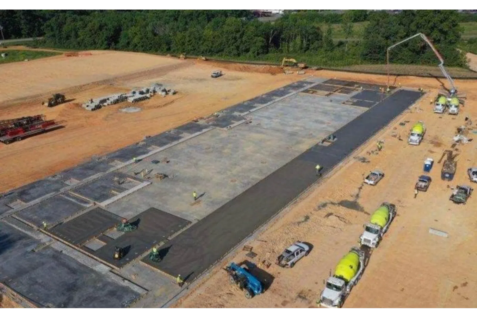 Aerial view of concrete foundation being poured at a large construction site with trucks and workers.