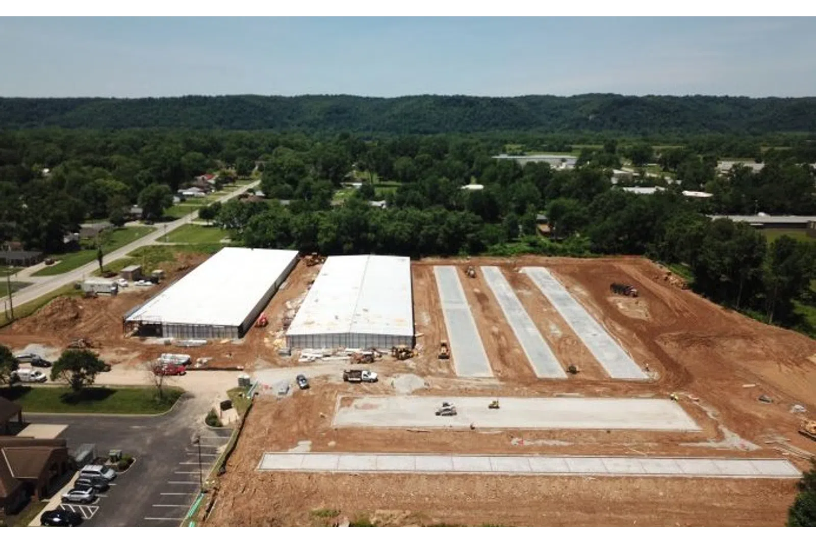 Aerial view of a construction site with two large warehouse buildings and concrete slabs surrounded by dirt and greenery.
