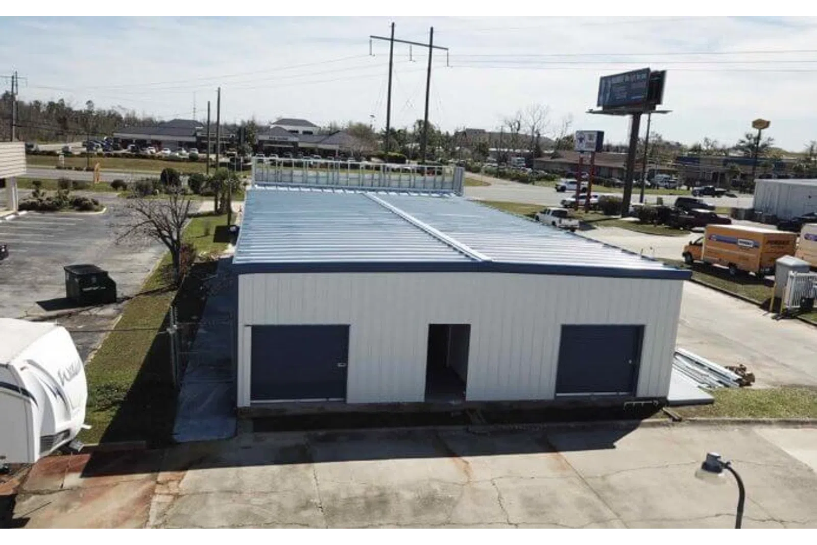 A white metal warehouse building with two large garage doors and an open entrance under a clear sky.
