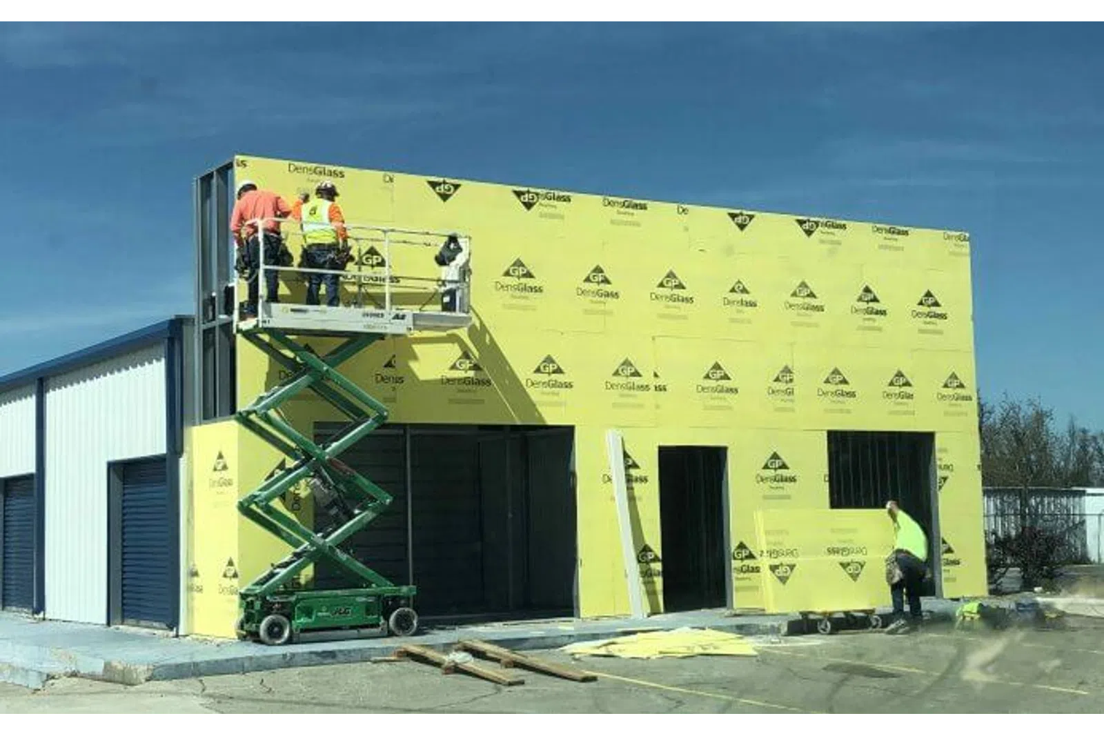Construction workers install yellow DensGlass sheathing on a commercial building under clear blue sky.