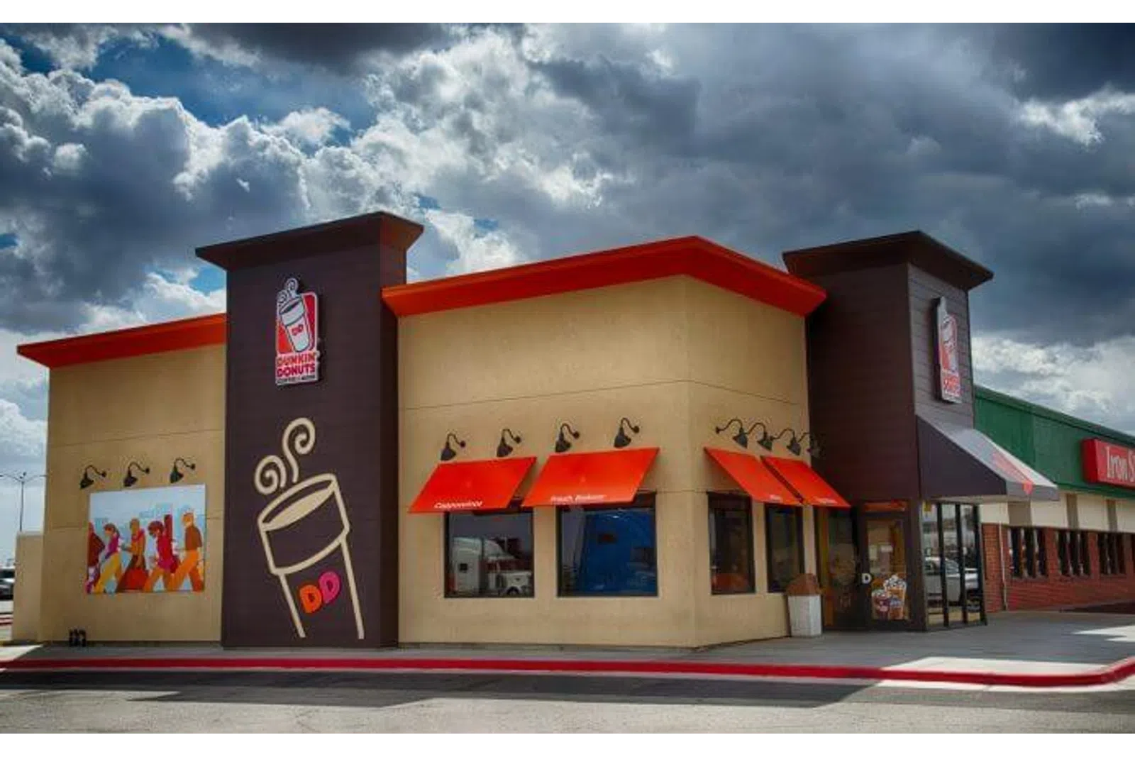 Dunkin' Donuts storefront with bold orange awnings and signage under a dramatic cloudy sky.