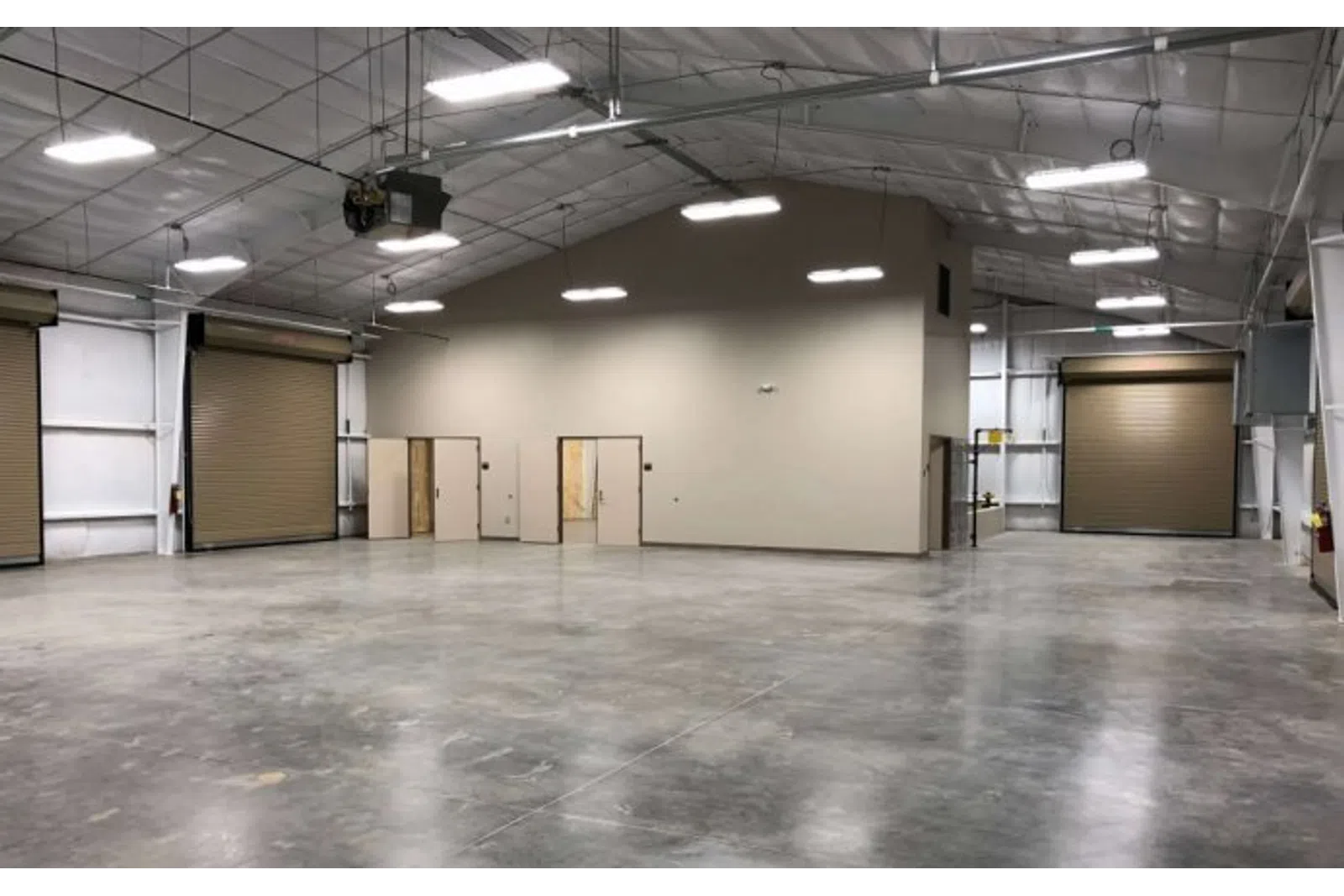 Spacious empty warehouse interior with polished concrete floor, high ceiling, and large roll-up doors.