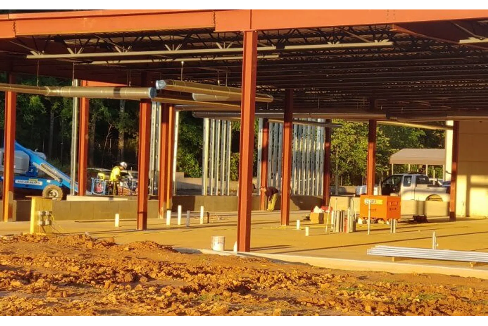 Steel framework and concrete foundation of a building under construction with workers and equipment visible