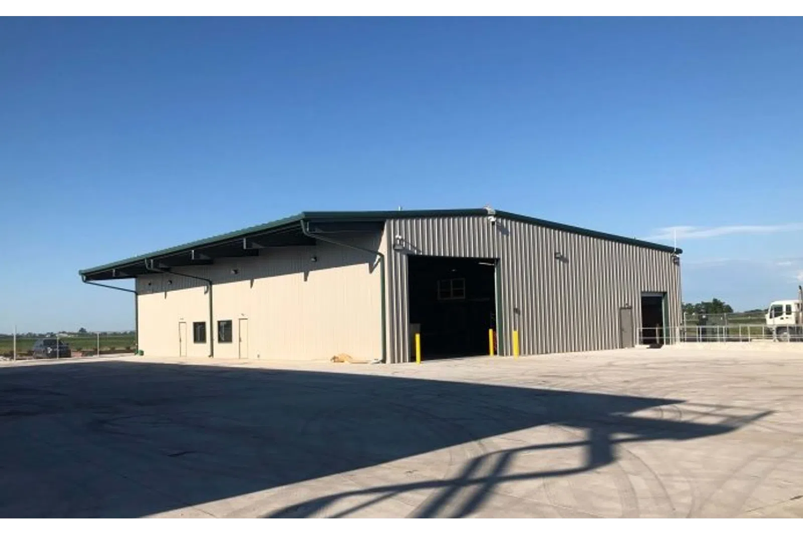 Large metal warehouse with beige and gray walls under a clear blue sky in an open paved area.