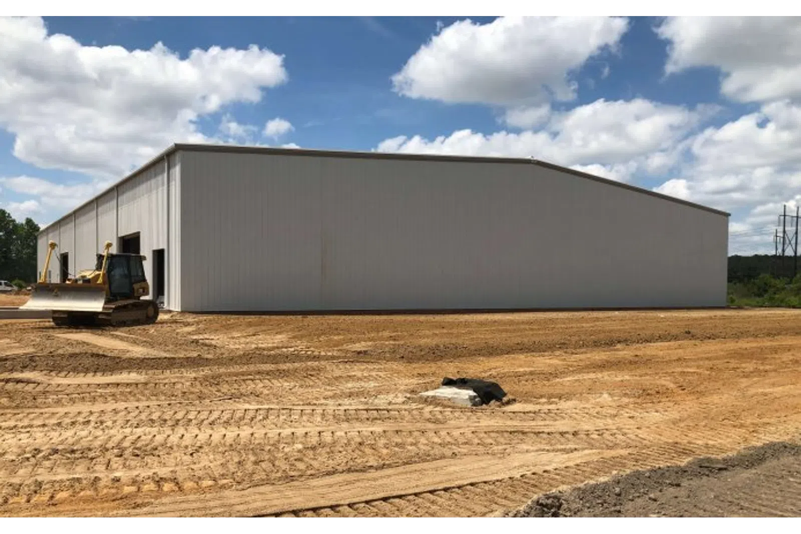 New large metal warehouse on construction site with bulldozer and clear blue sky with clouds