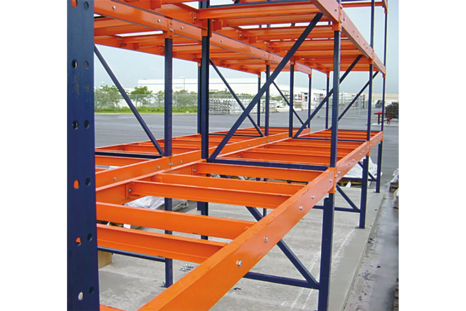Orange and blue industrial metal storage rack shelving outdoors on concrete surface near warehouse.