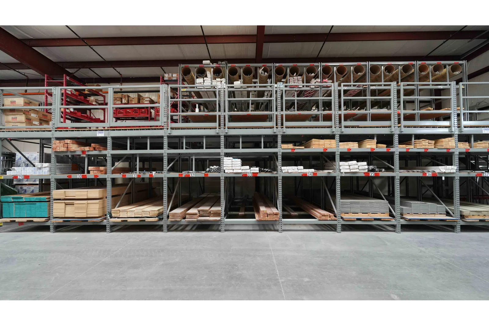 Organized warehouse shelves stocked with wood planks, pipes, and building materials in a large industrial space