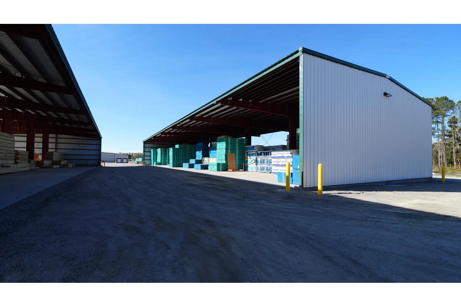 Outdoor warehouse with stacks of construction materials under metal roof structures on a clear day