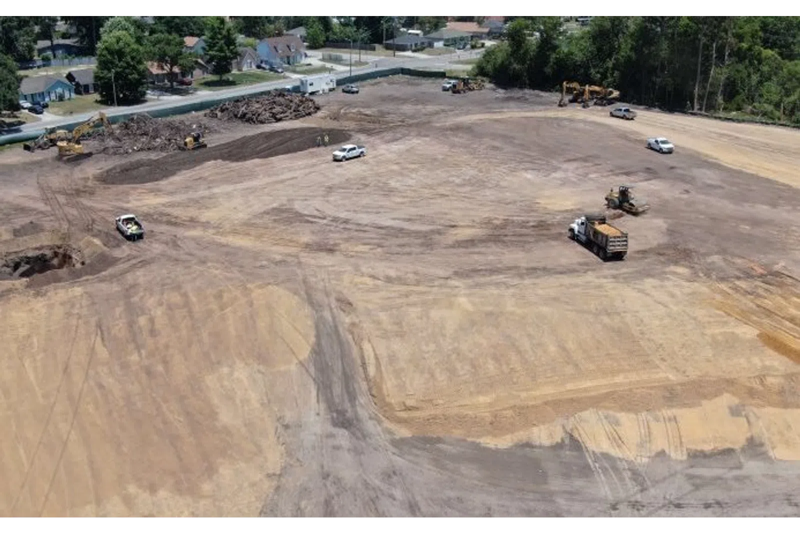 Aerial view of a large dirt construction site with machinery and trucks working on land clearing near a residential area