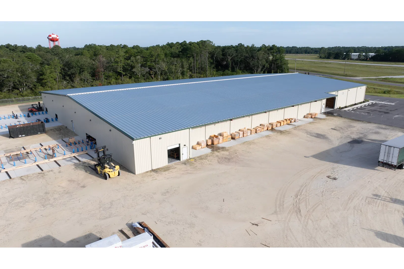 Aerial view of a large metal warehouse with a forklift and stacked pallets in a rural setting