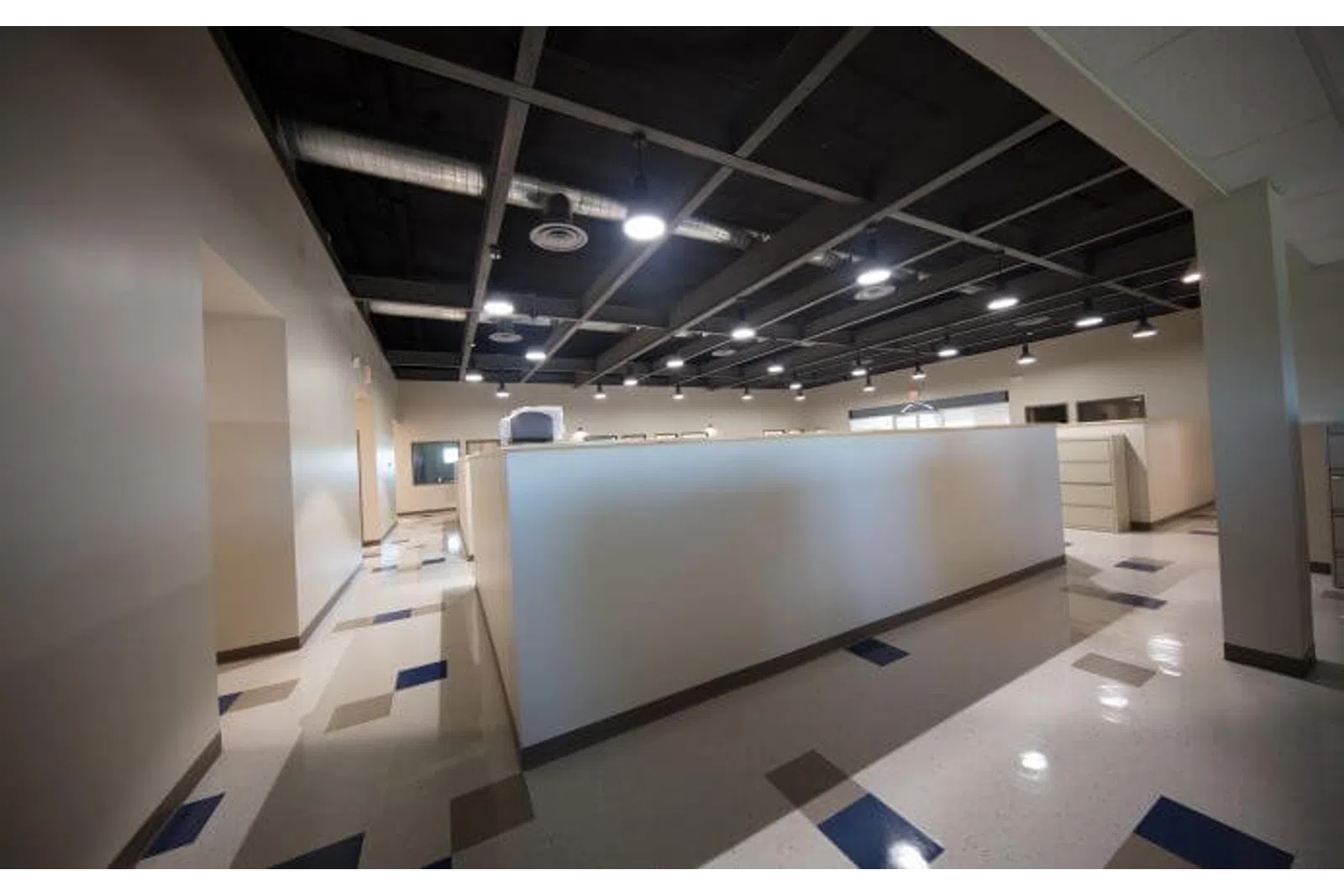 Modern empty office space with cubicles, polished floors, and overhead industrial lighting.