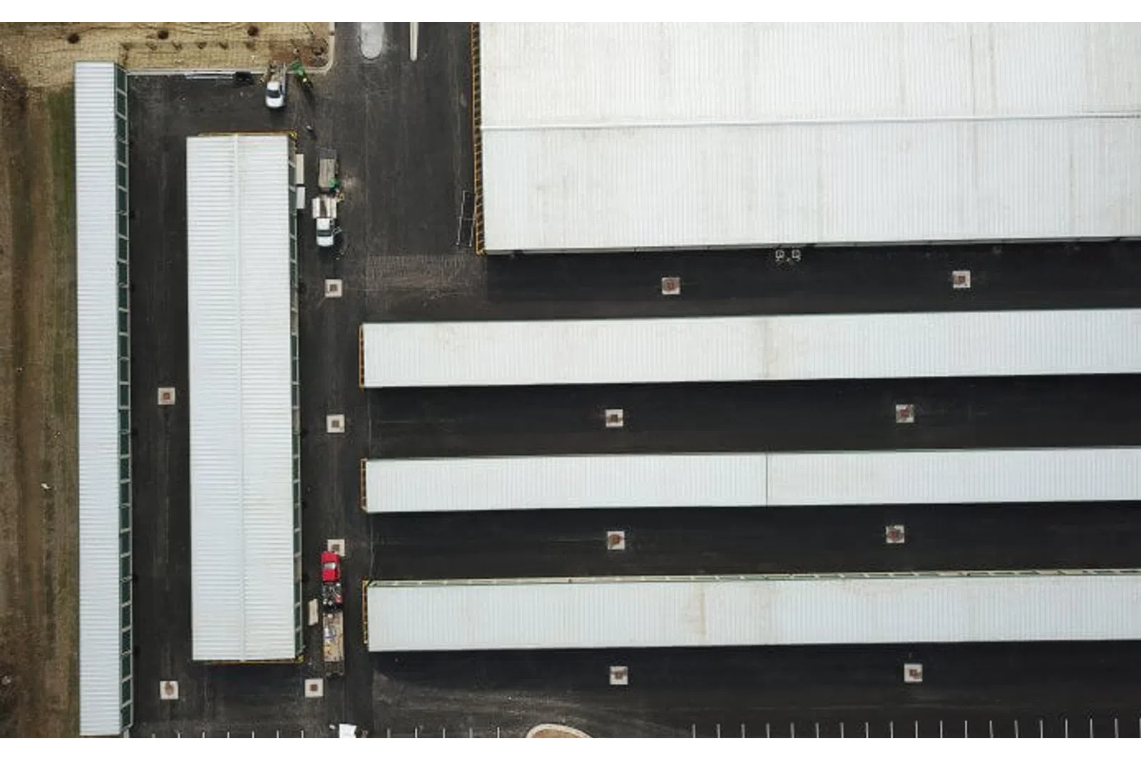 Aerial view of multiple long white-roofed warehouse buildings with black asphalt roads and parking areas.