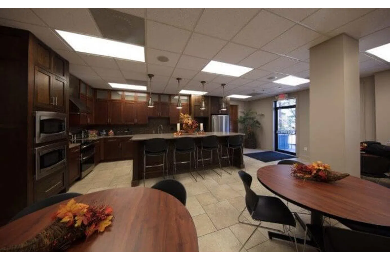 Modern kitchen and dining area with dark wood cabinets, island seating, and round tables with fall centerpieces.