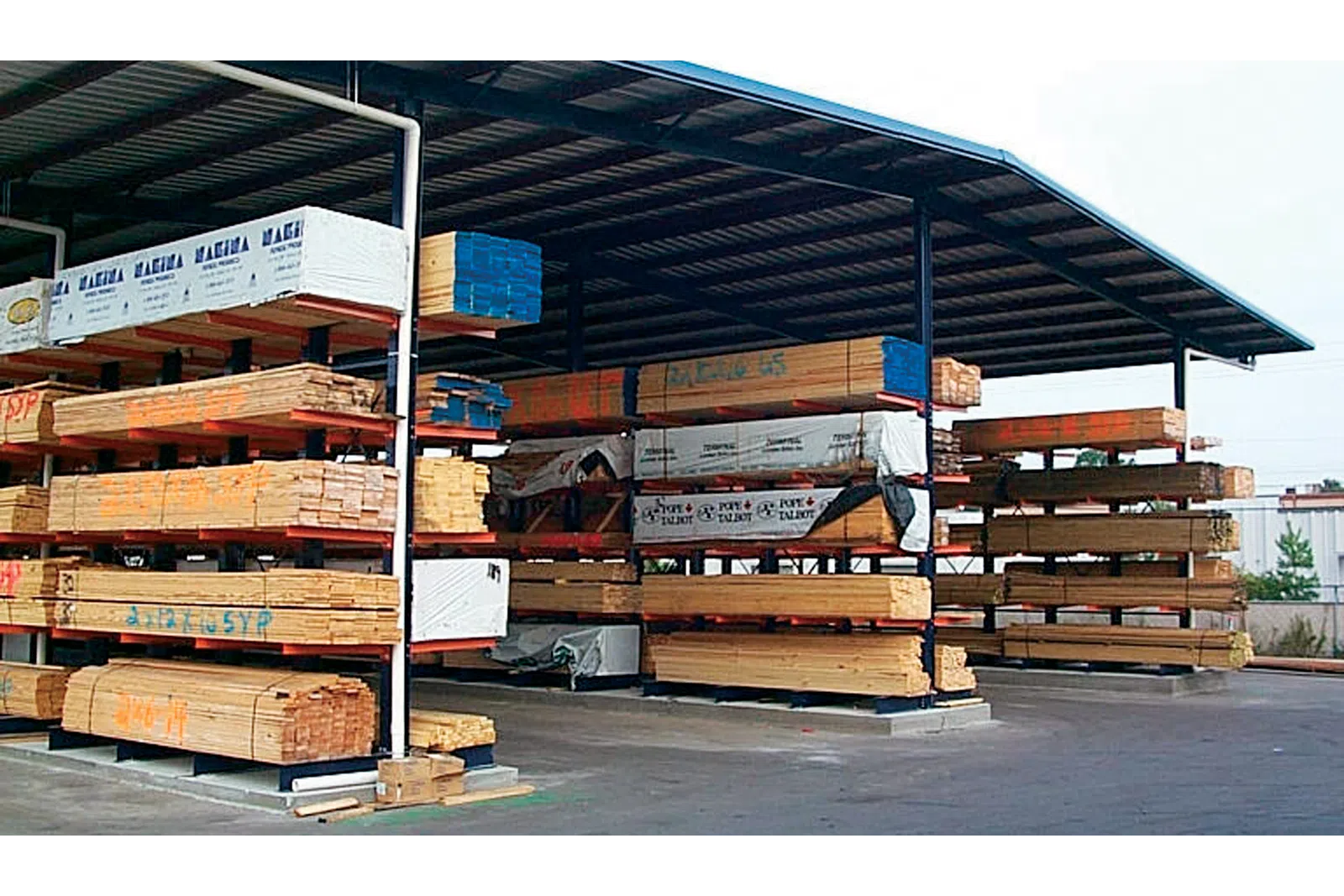 Covered outdoor lumber storage with multiple stacks of wooden planks organized on metal racks.