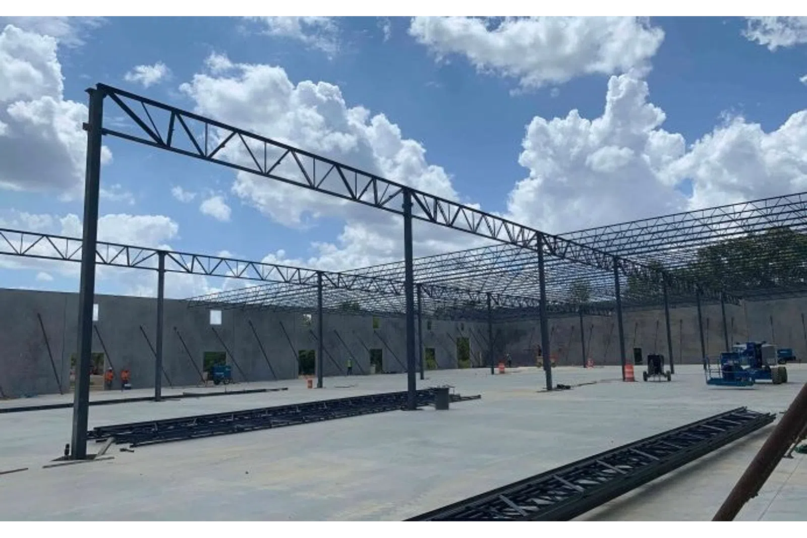 Steel framework construction in progress inside a large building under a cloudy blue sky.