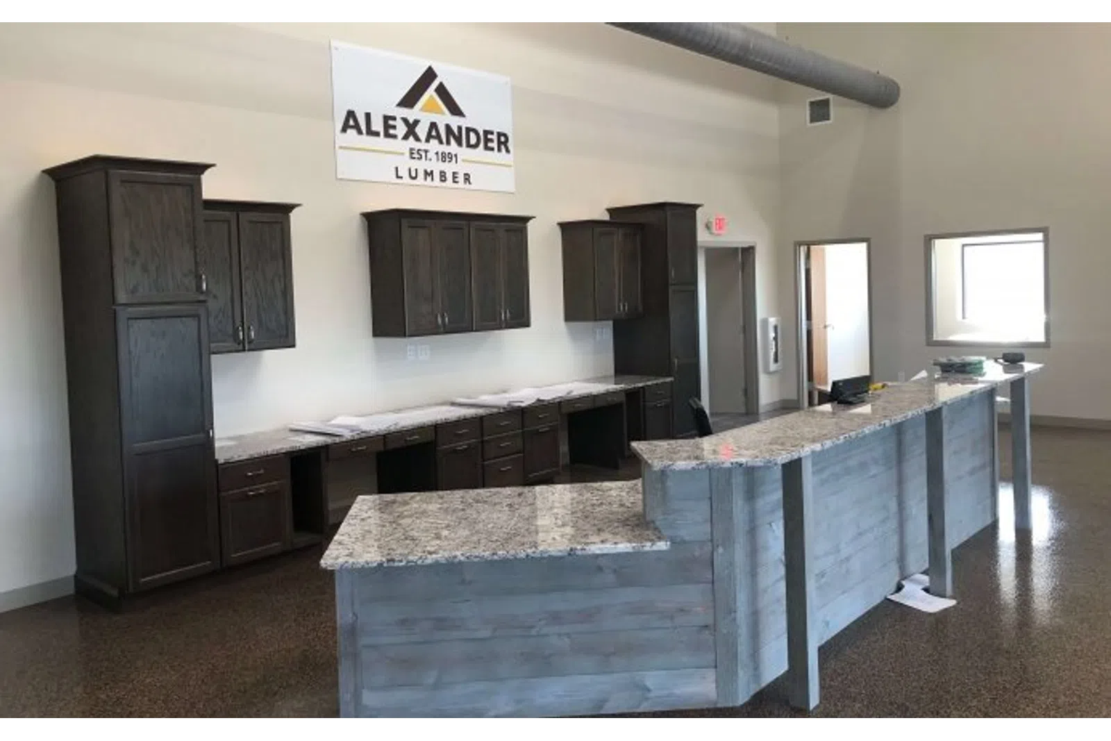 Modern office interior with granite countertop reception desk and dark wood cabinets under an Alexander Lumber sign.
