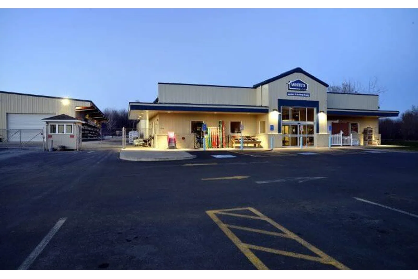 Exterior view of a well-lit commercial building with parking lot and signage at dusk.