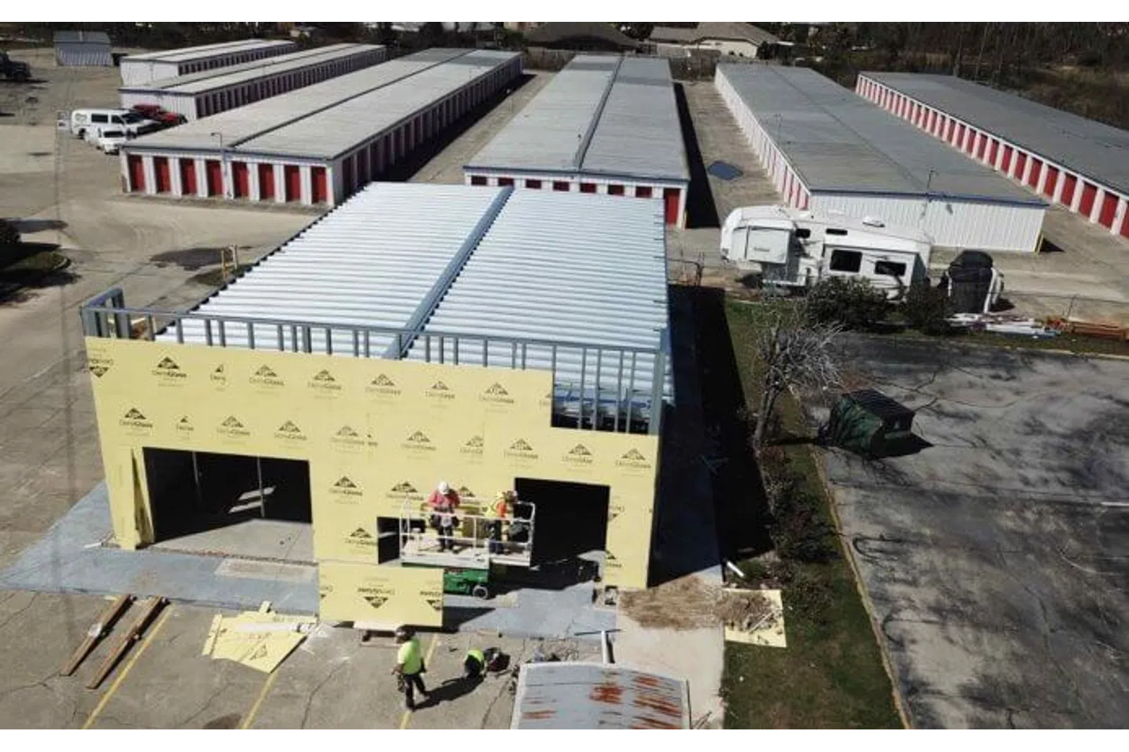 Construction workers building a prefab storage unit building near multiple storage units with red doors.