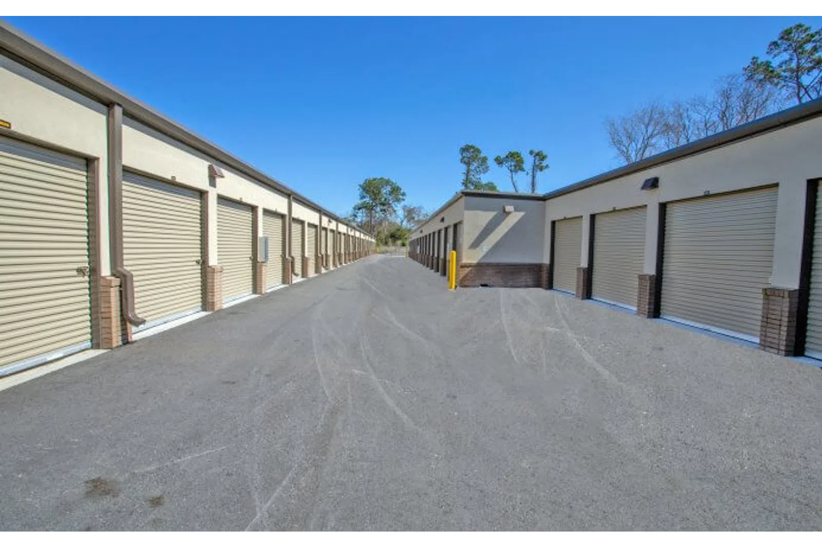 Outdoor self-storage facility with multiple beige roll-up garage doors under a clear sky