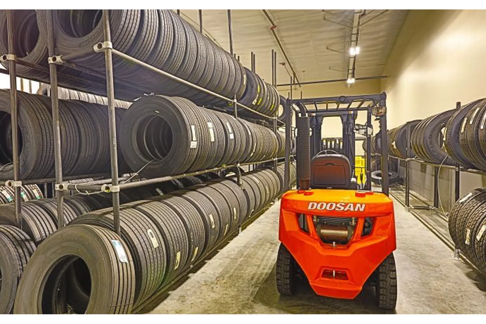 Red Doosan forklift in a warehouse aisle surrounded by shelves stacked with black tires