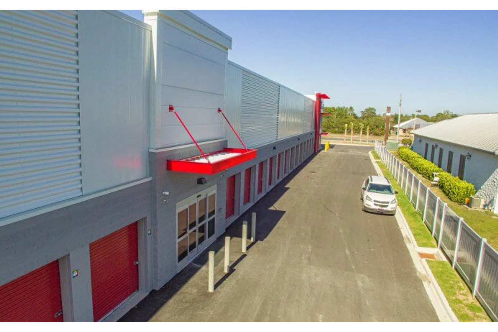 Modern industrial building with red accents, large windows, and a parked white vehicle on a paved driveway.