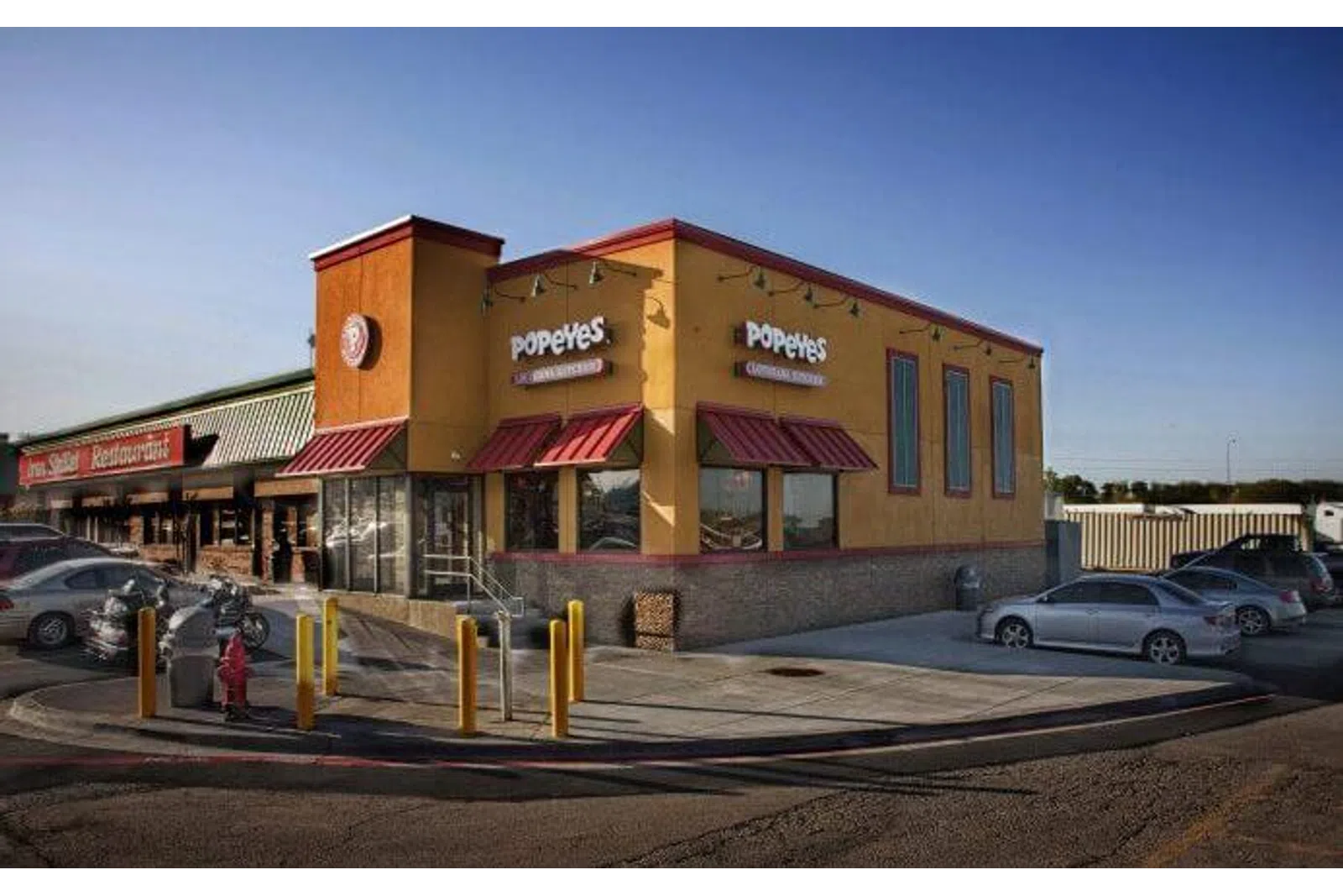 Popeyes Louisiana Kitchen restaurant building with cars parked outside on a clear day.