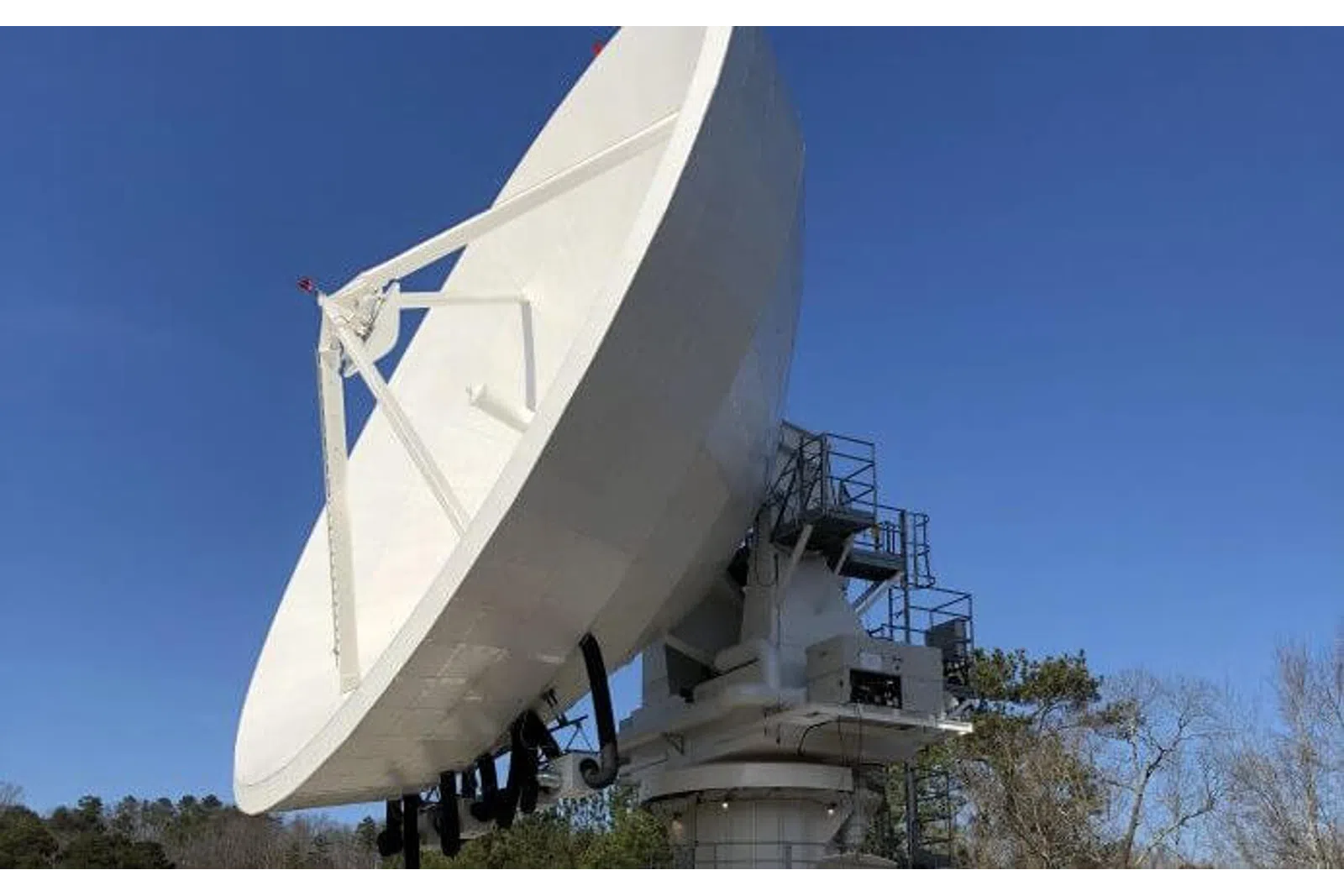 Large white satellite dish antenna against clear blue sky with trees in the background