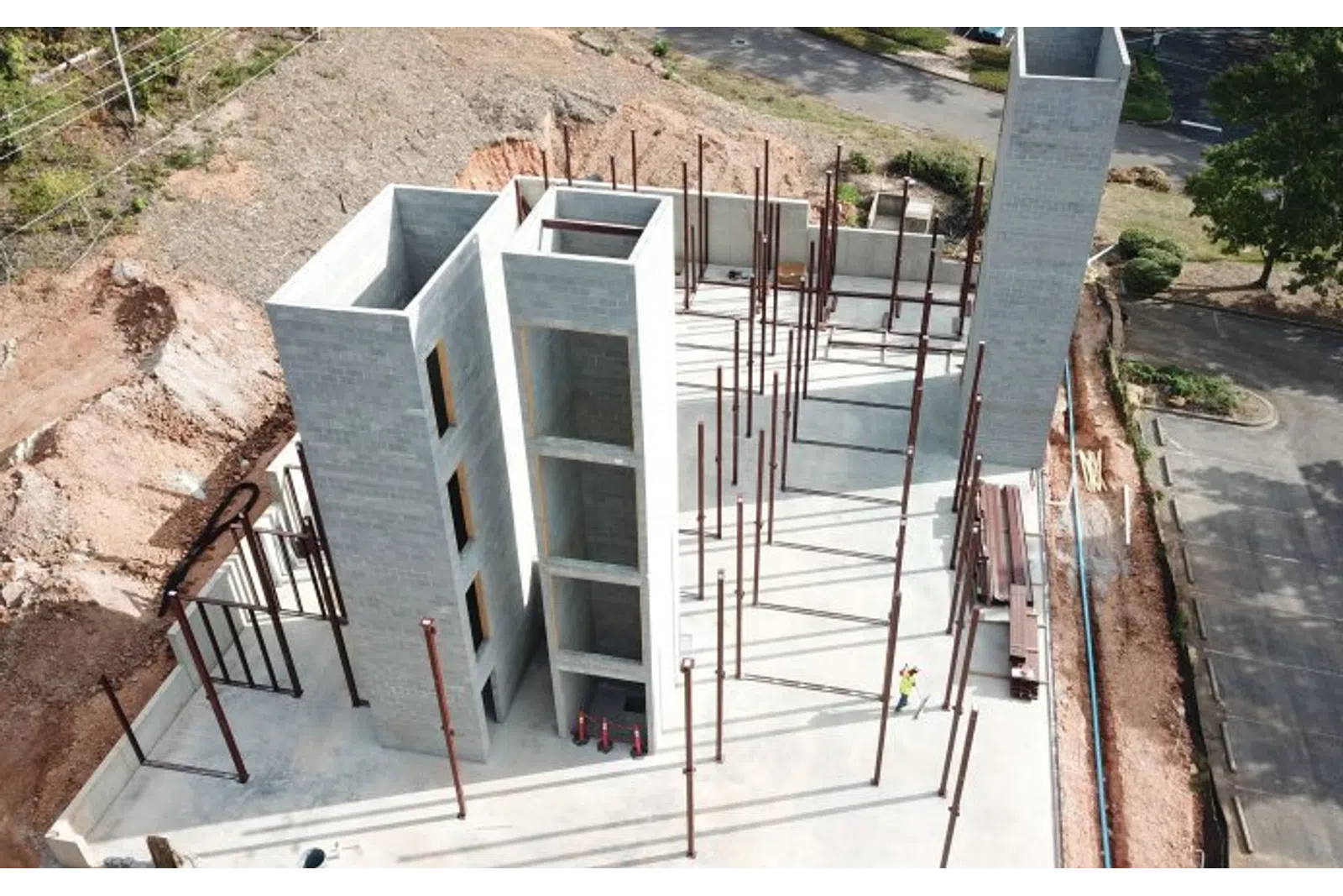 Aerial view of gray concrete building under construction with exposed steel beams and workers onsite.