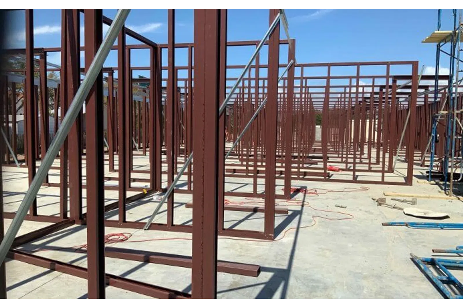 Steel framework structure under construction on concrete floor with clear blue sky background.