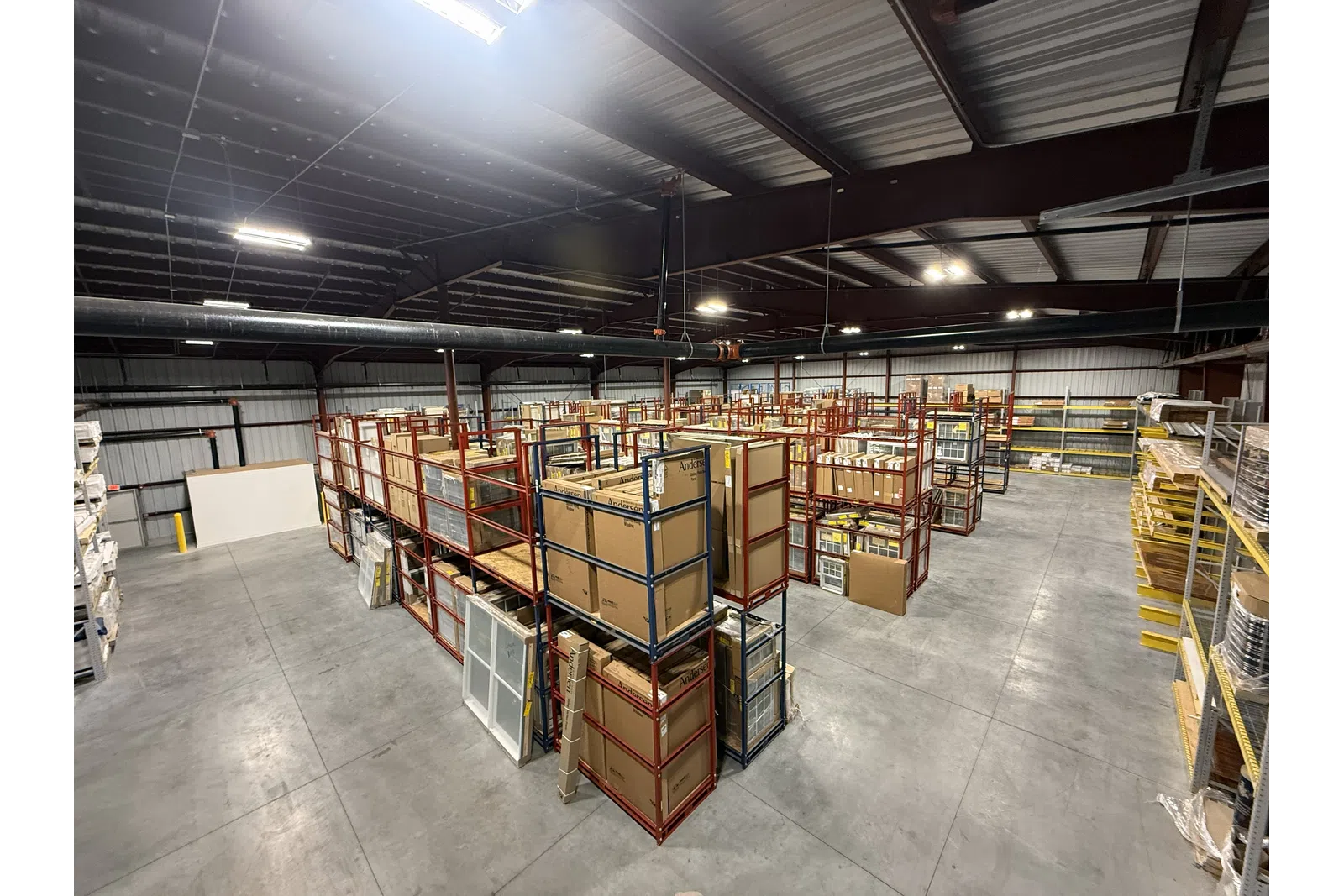 Spacious warehouse with metal shelving racks storing boxed inventory and building materials under bright ceiling lights