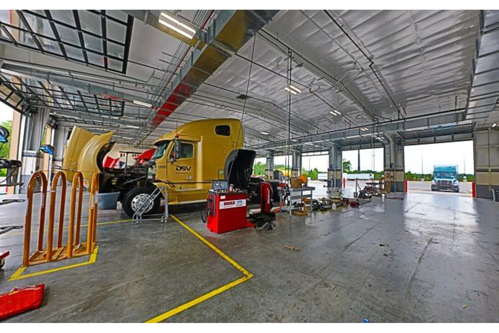 Interior of a large truck maintenance garage with a yellow semi truck being serviced under bright lighting.