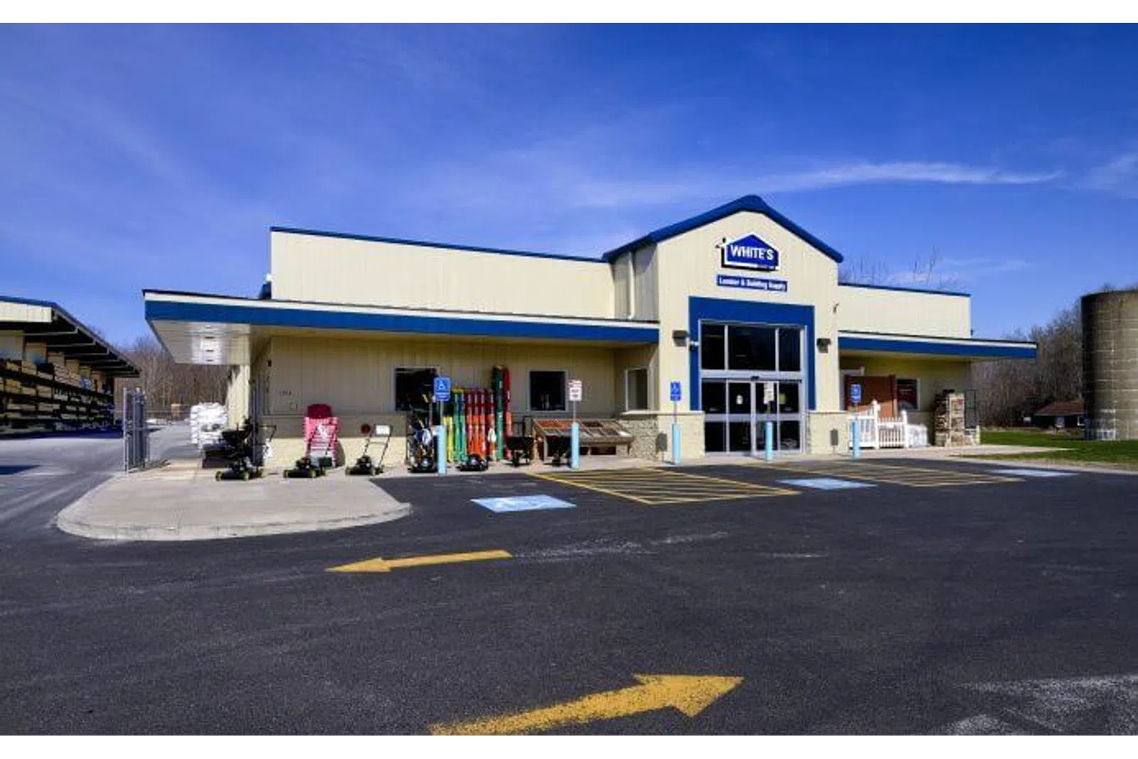Exterior view of White's Lumber and Building Supply store with equipment and handicap parking under a clear blue sky.