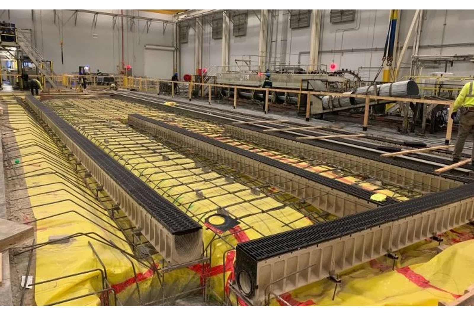 Indoor construction site with insulated trenches and steel reinforcements for concrete pouring in progress.