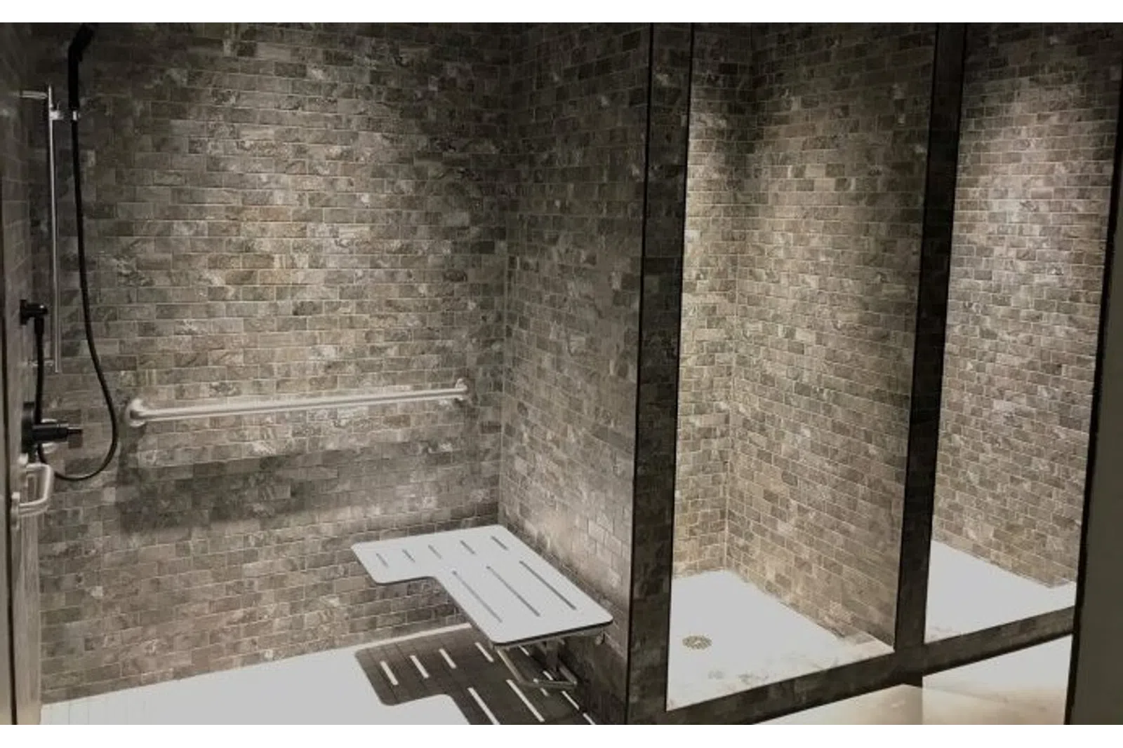 Accessible shower with foldable seat, grab bar, and dark tiled walls in a modern bathroom space.