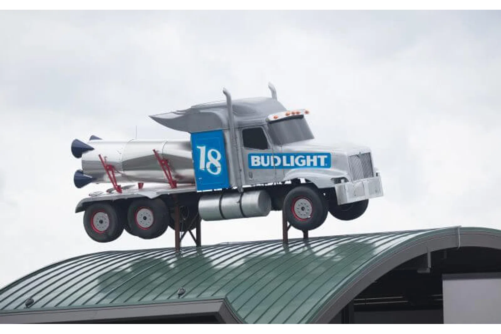 Silver Bud Light truck with rocket detail mounted on a curved green rooftop against a gray sky.