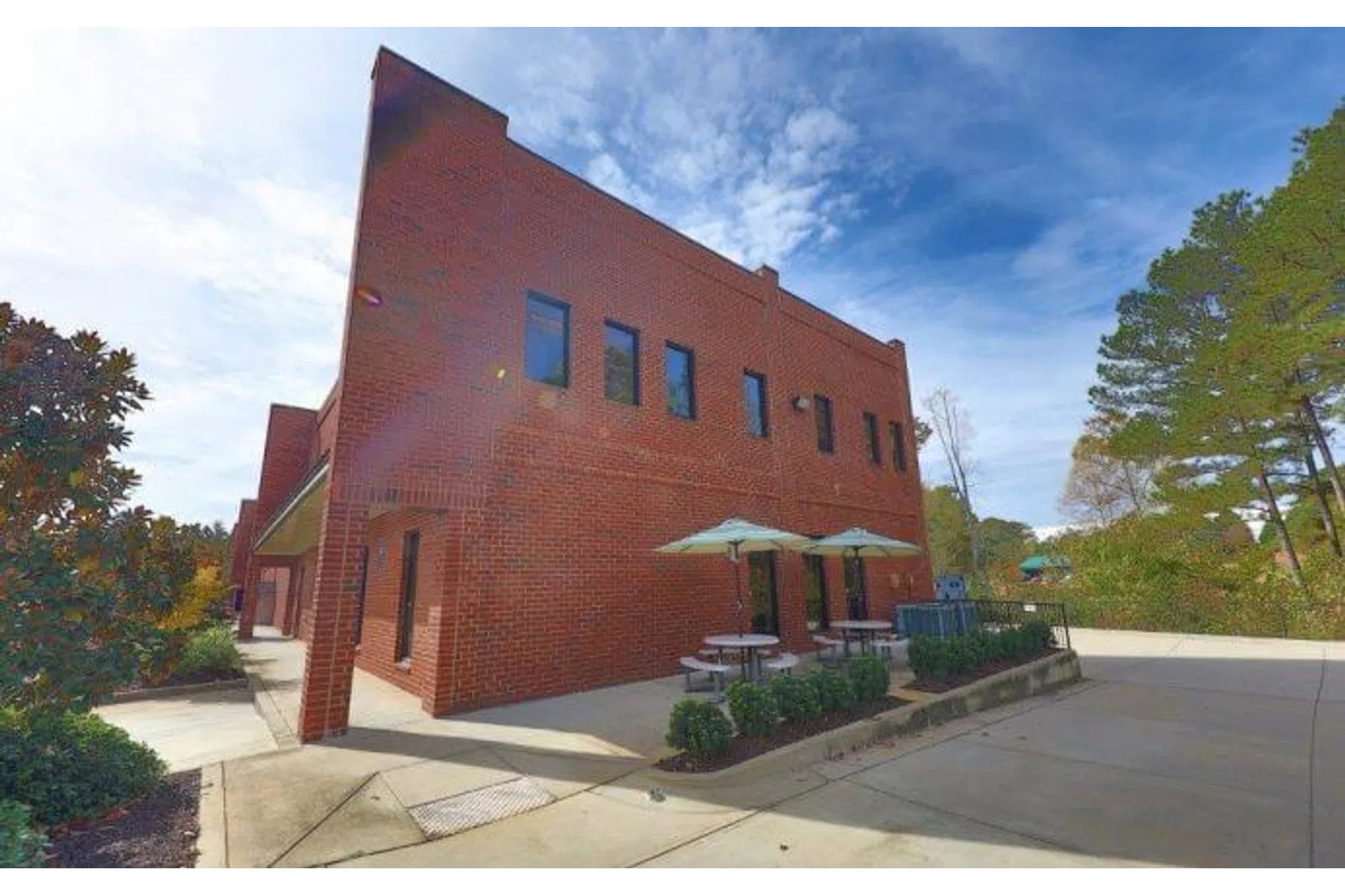 Two-story red brick building with outdoor patio tables and umbrellas under a blue sky.
