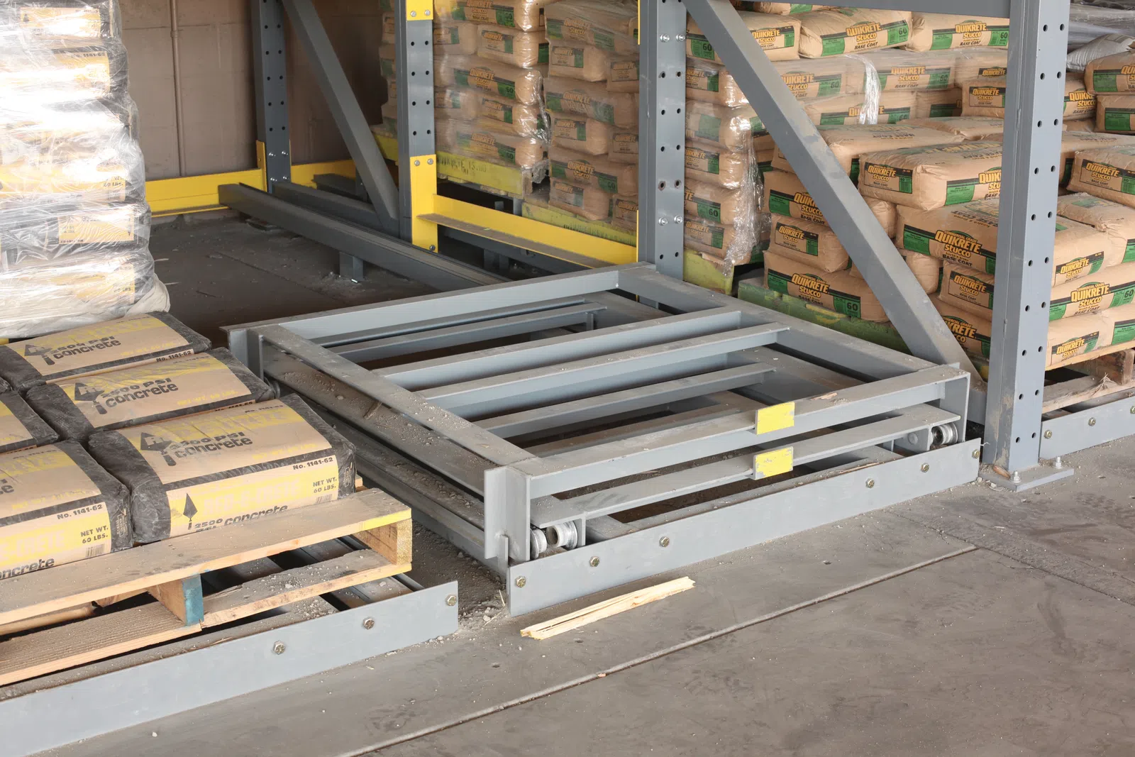 Stacked cement bags on pallets in warehouse storage with metal shelving and industrial floor.