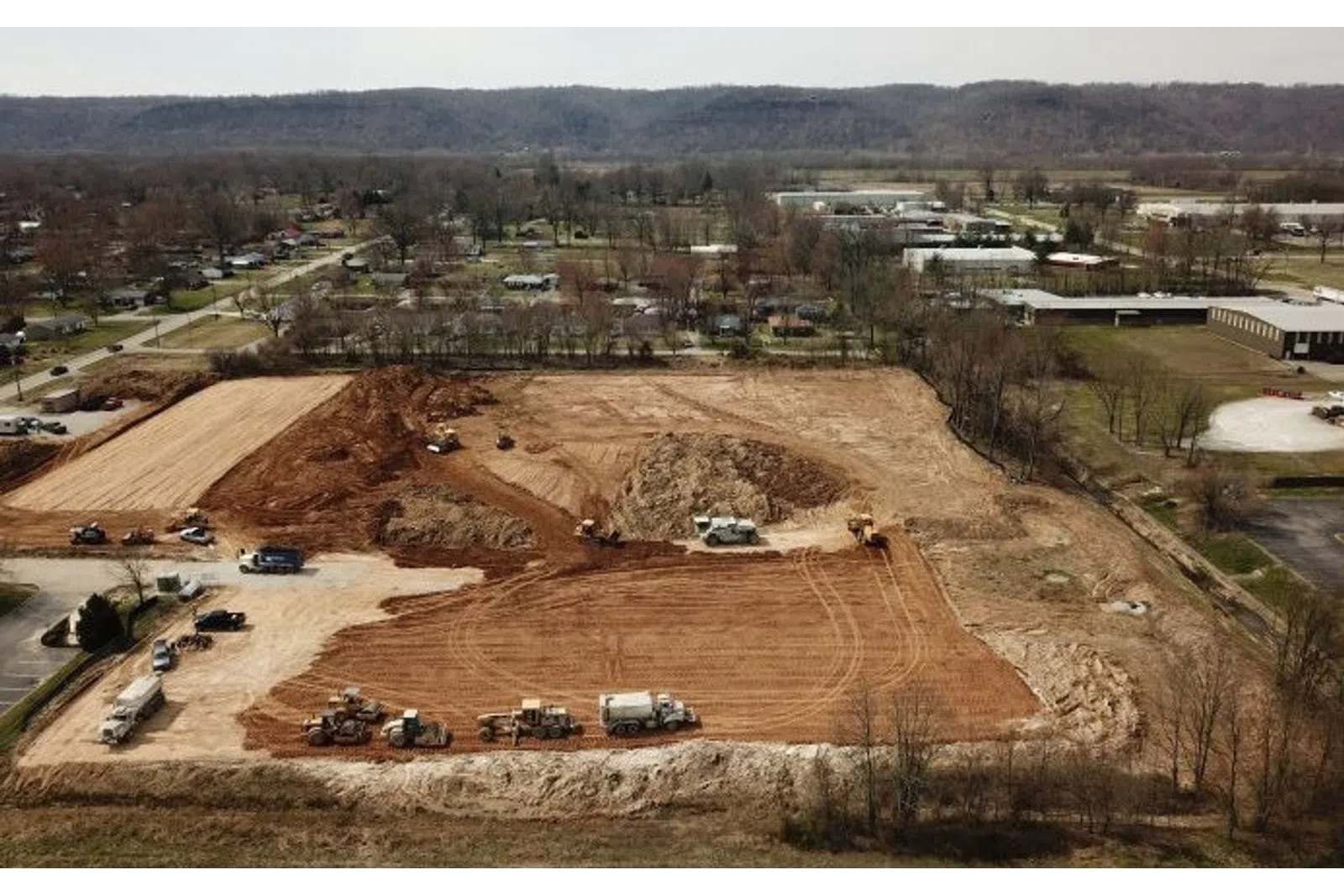 Aerial view of large construction site with trucks and machinery preparing land in a suburban area.