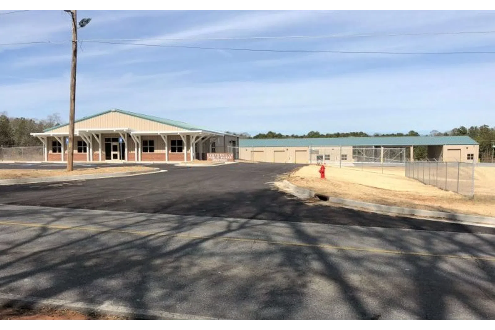 Newly constructed single-story building with green roof, large paved parking lot, and fenced area under clear sky.