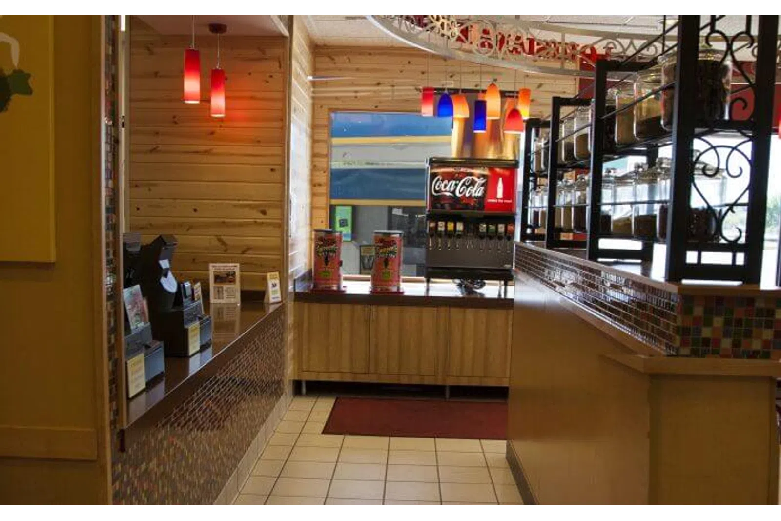 Interior of a restaurant self-service drink station with Coca-Cola dispenser and colorful hanging lights.