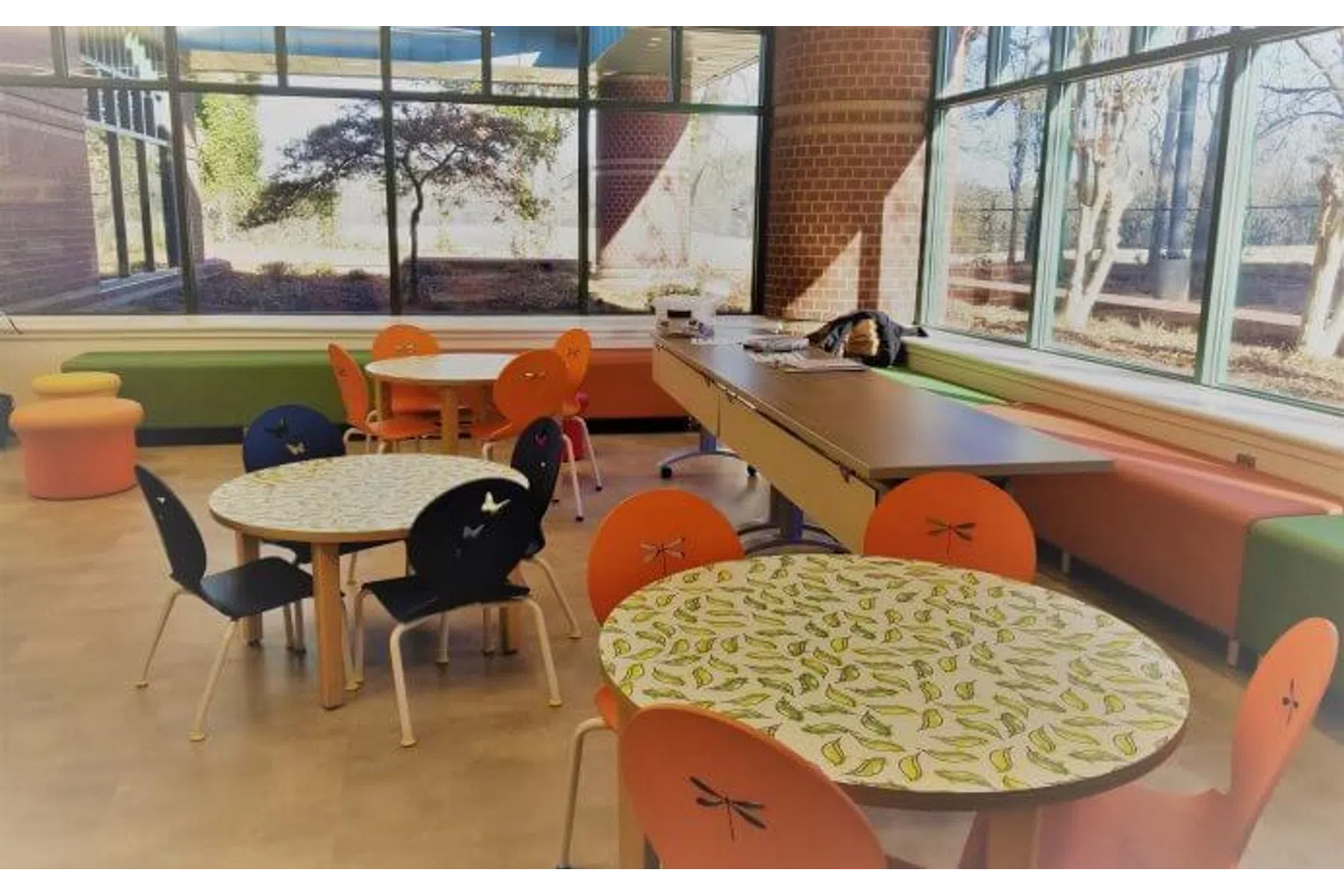 Bright modern room with round tables featuring leaf designs and colorful chairs under large windows with natural light.