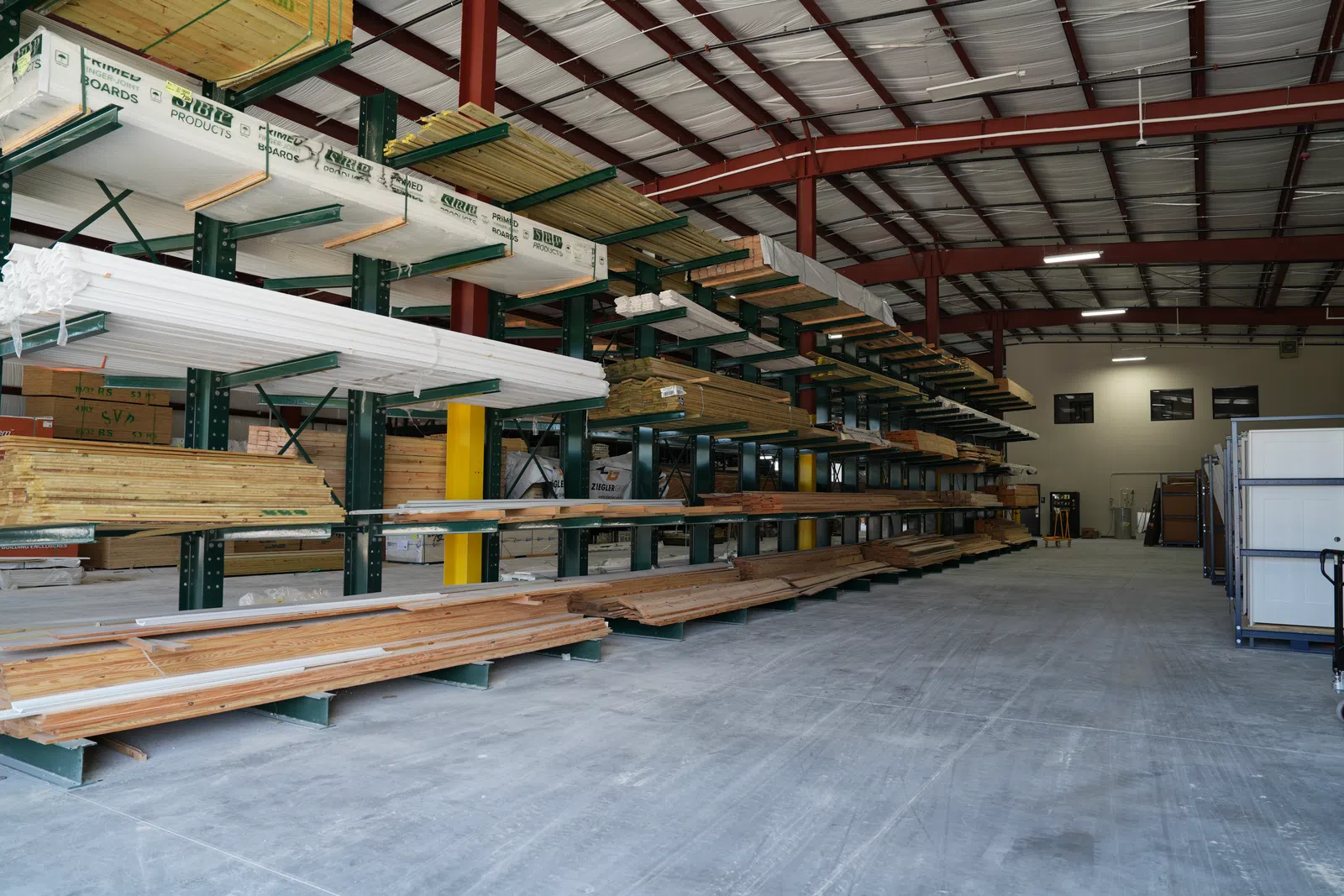 Interior view of a lumber warehouse with stacked wood planks and boards on industrial shelves.