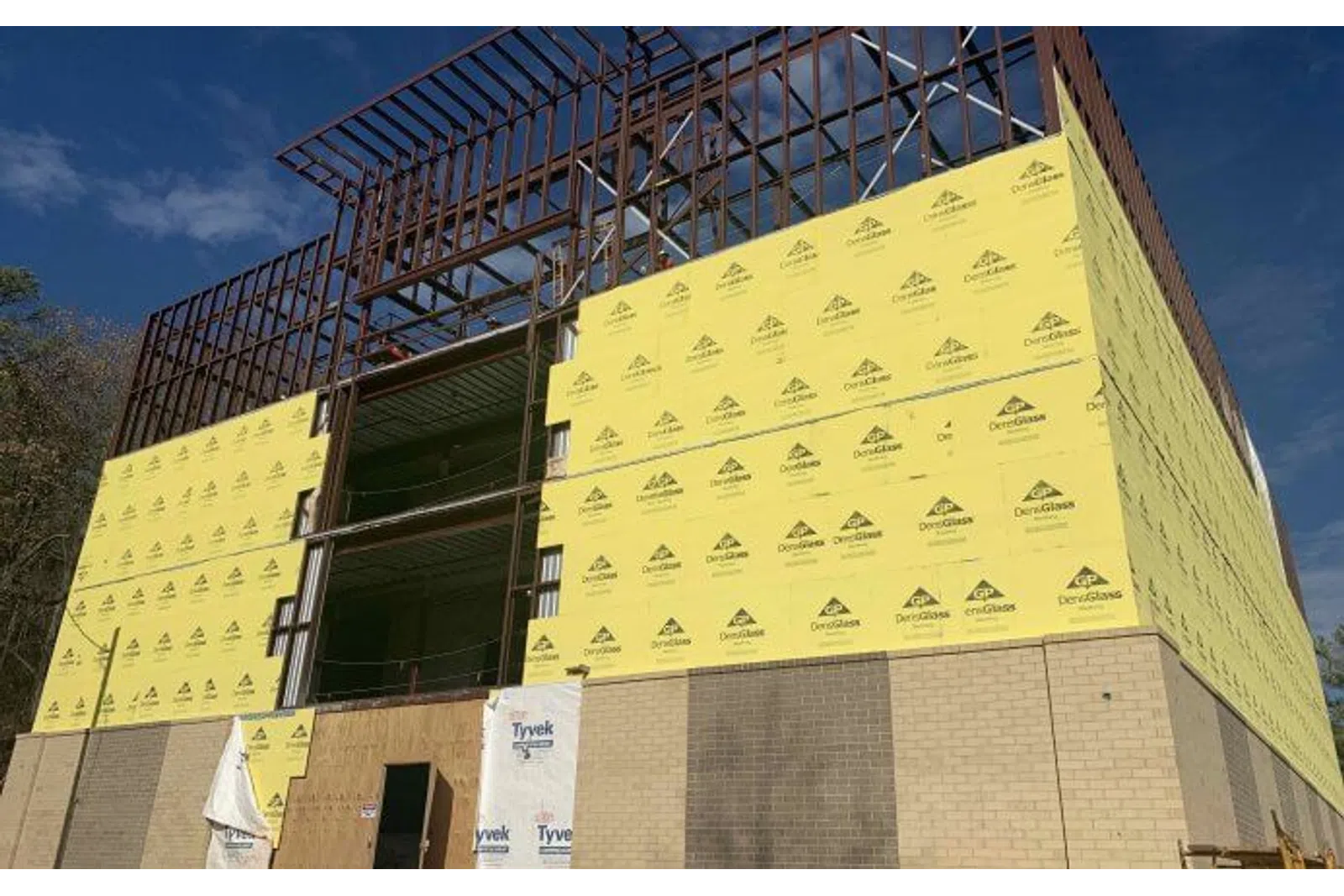 Construction site with steel framework and yellow exterior sheathing panels under a clear blue sky