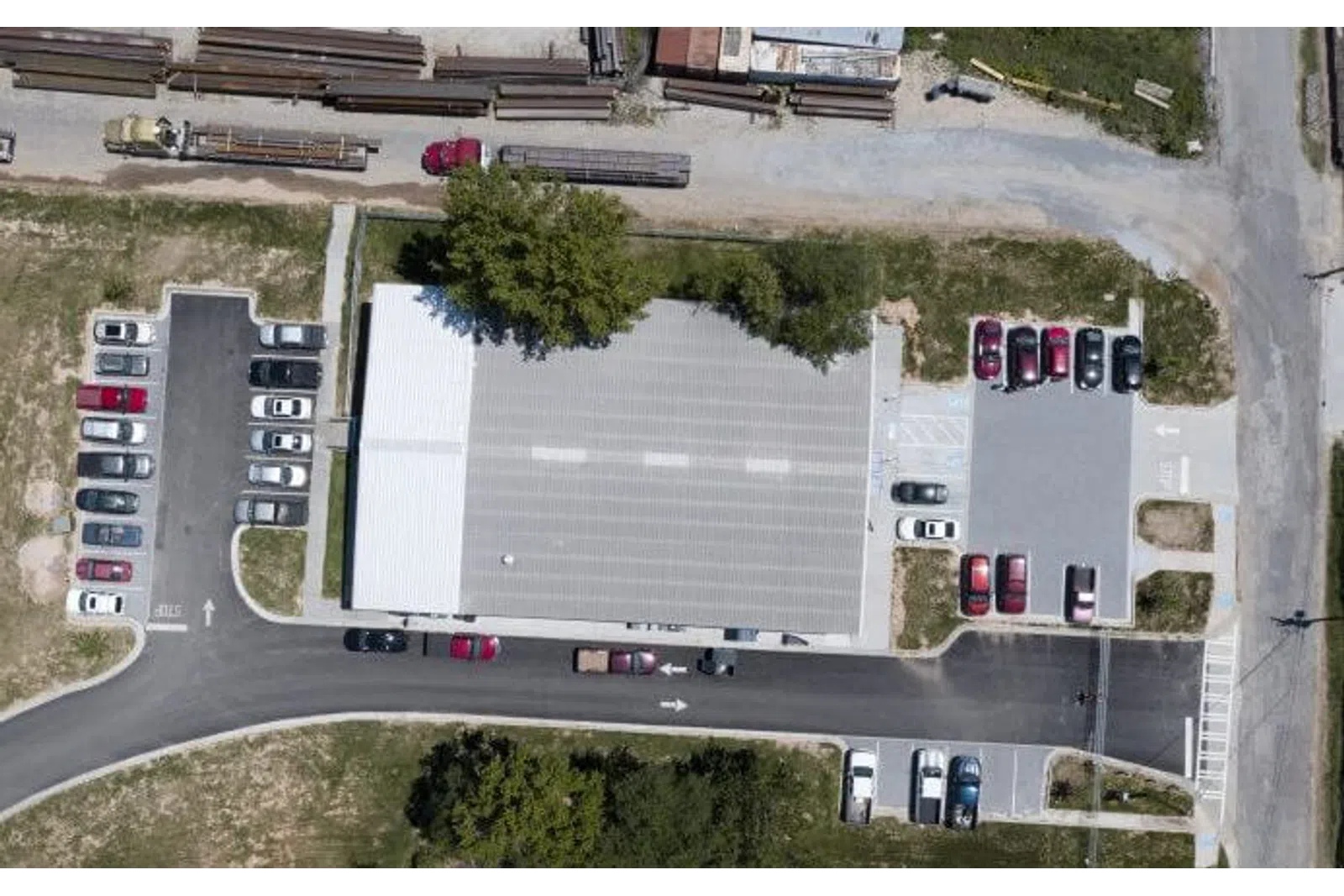 Aerial view of a large building with multiple parked cars and green trees surrounding the area.