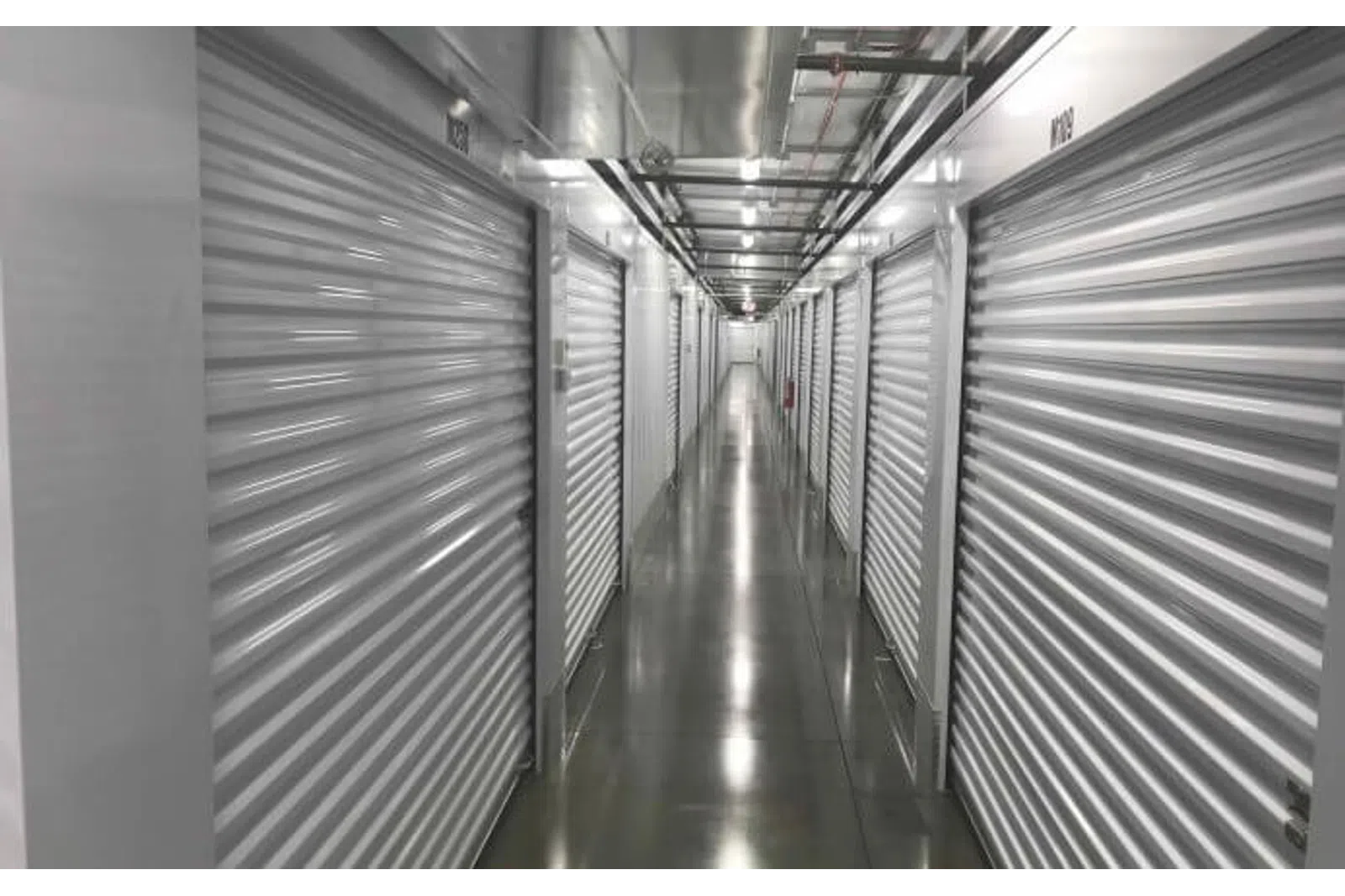 Long indoor hallway with metal roll-up doors on both sides and polished concrete floor in a storage facility