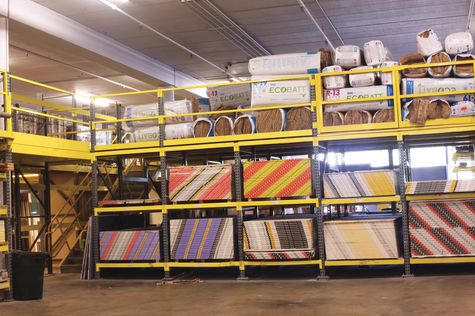 Industrial warehouse shelving stocked with insulation materials and construction supplies under bright lighting.