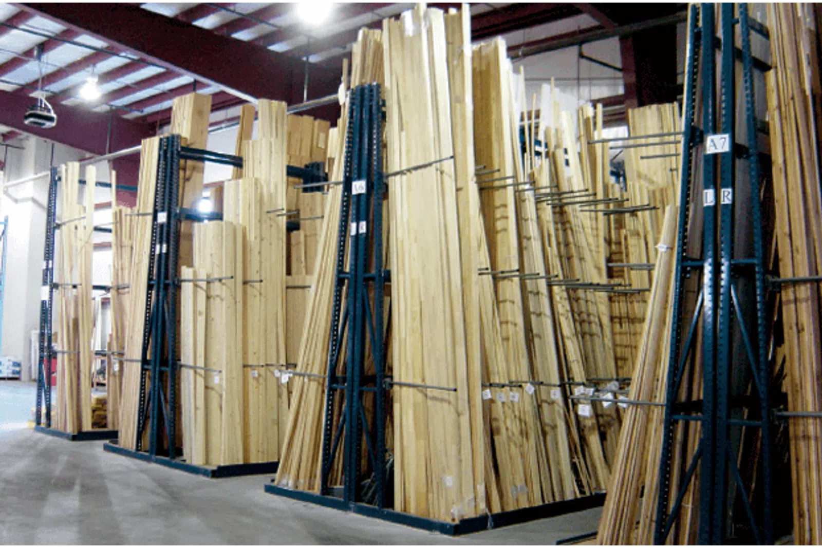 Large stacks of wooden planks stored upright in an organized warehouse with high ceilings and bright lighting