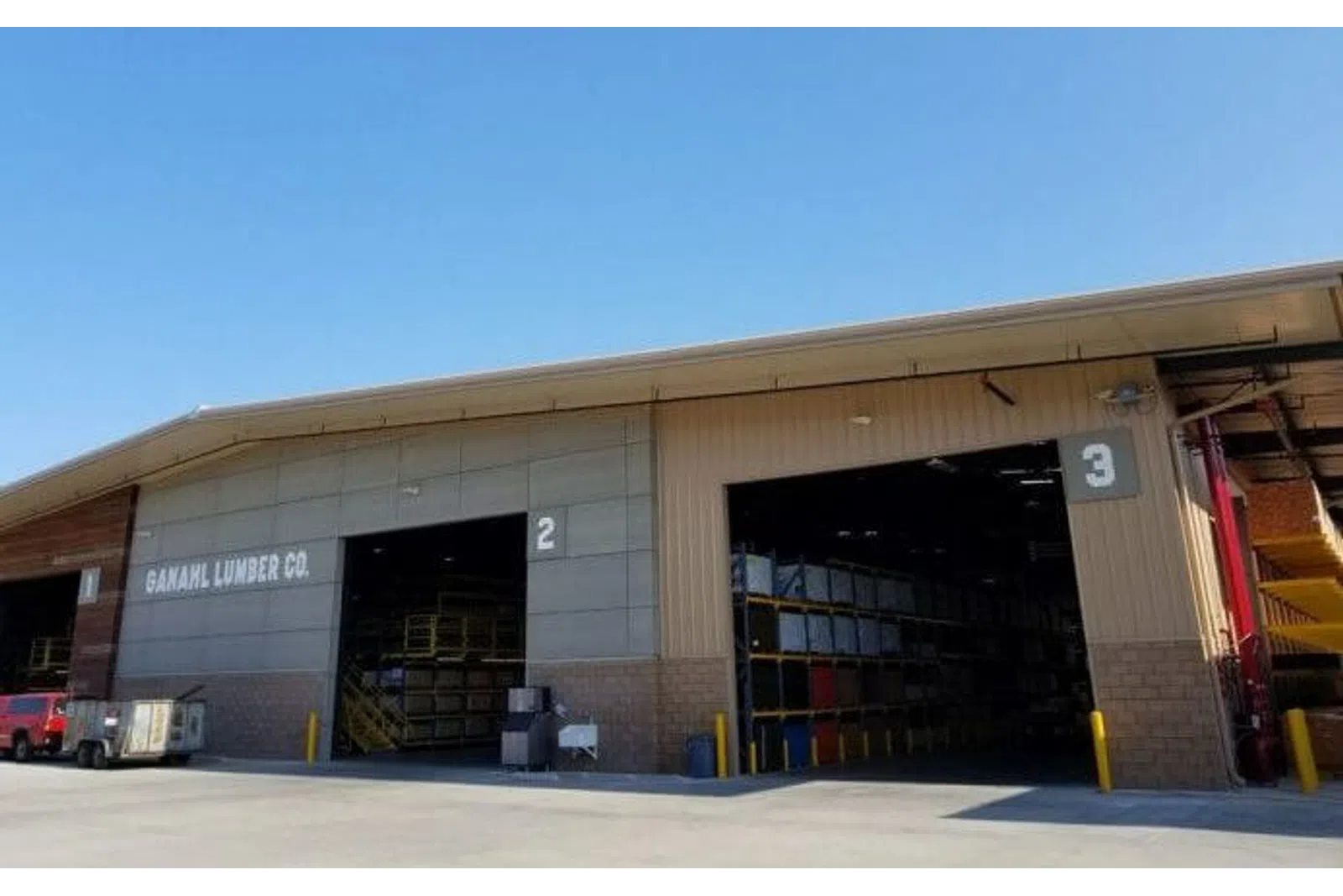 Exterior view of Ganahl Lumber Co. warehouse with open bays numbered 2 and 3 under clear blue sky.