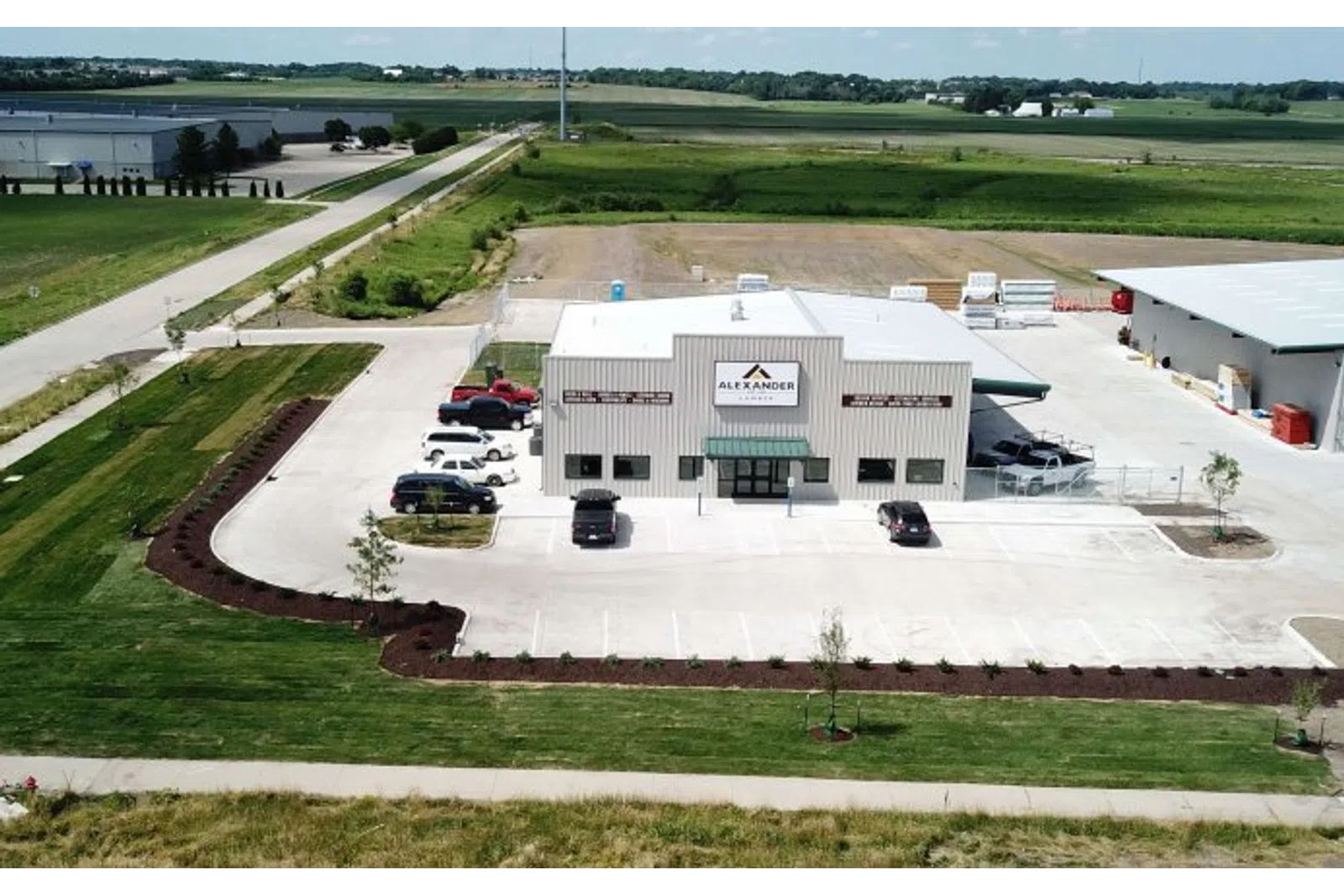 Aerial view of Alexander building with parking lot, surrounding greenery, and rural landscape under blue sky.