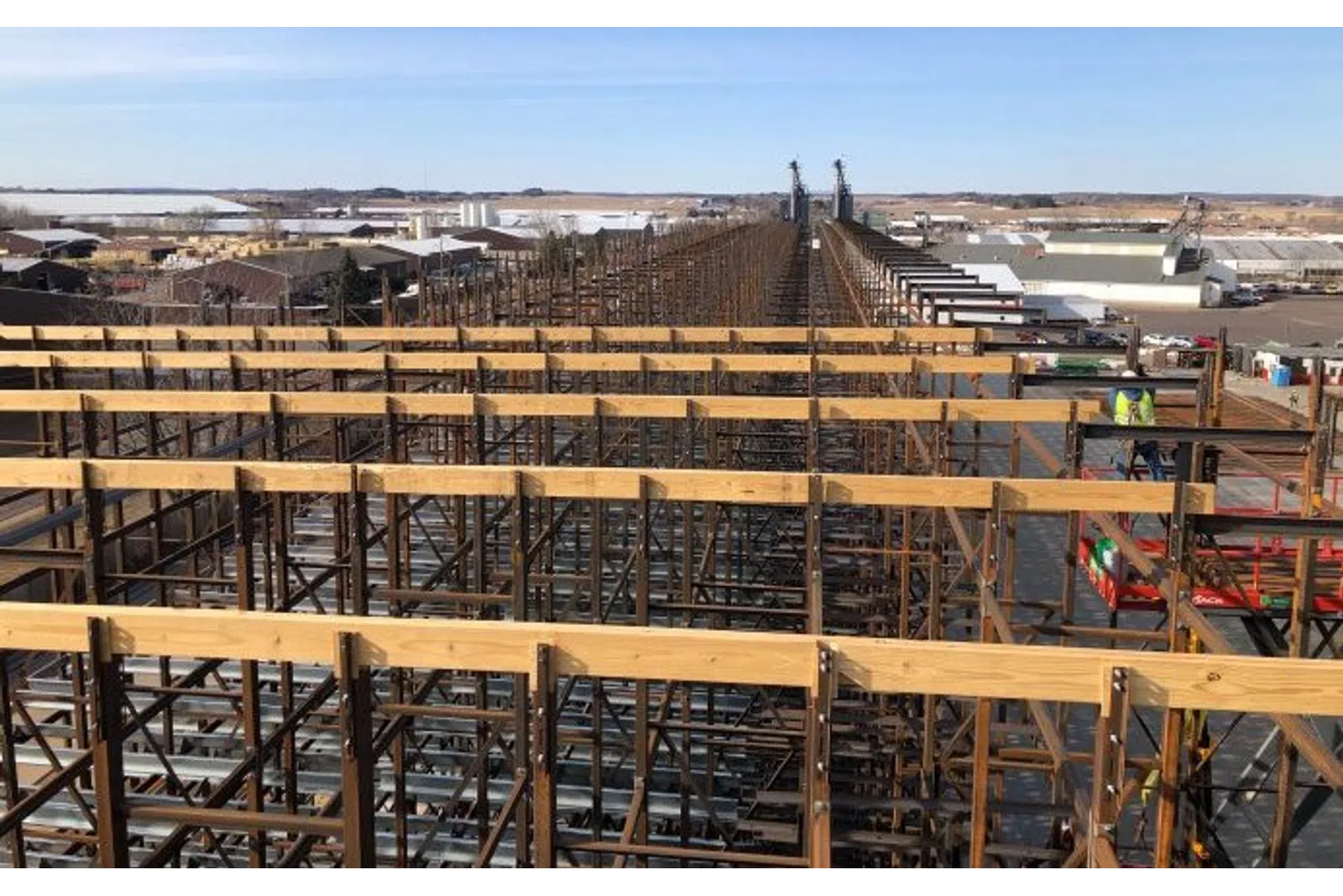 Large industrial wooden scaffolding structure under clear sky with workers and buildings in the background
